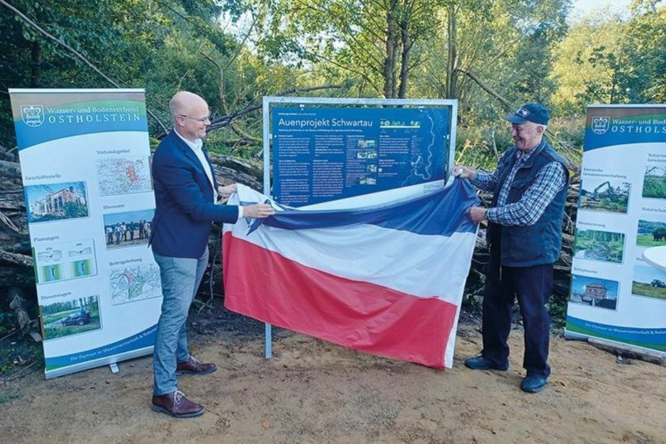 Gemeinsam enthüllen Umweltminister Tobias Goldschmidt (l.) und Robert Muus, Verbandsvorsteher des Wasser- und Bodenverbandes Schwartau, die Infotafel.