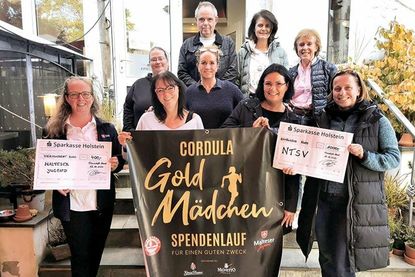 Heike Baroth-Blume, Daniela Imkamp und Petra Oesau von den „Goldmädchen“ (hinter dem Banner von links) bei der obligatorischen Scheckübergabe an die Vertreter vom NTSV Strand 08 und der Malteser-Jugend.