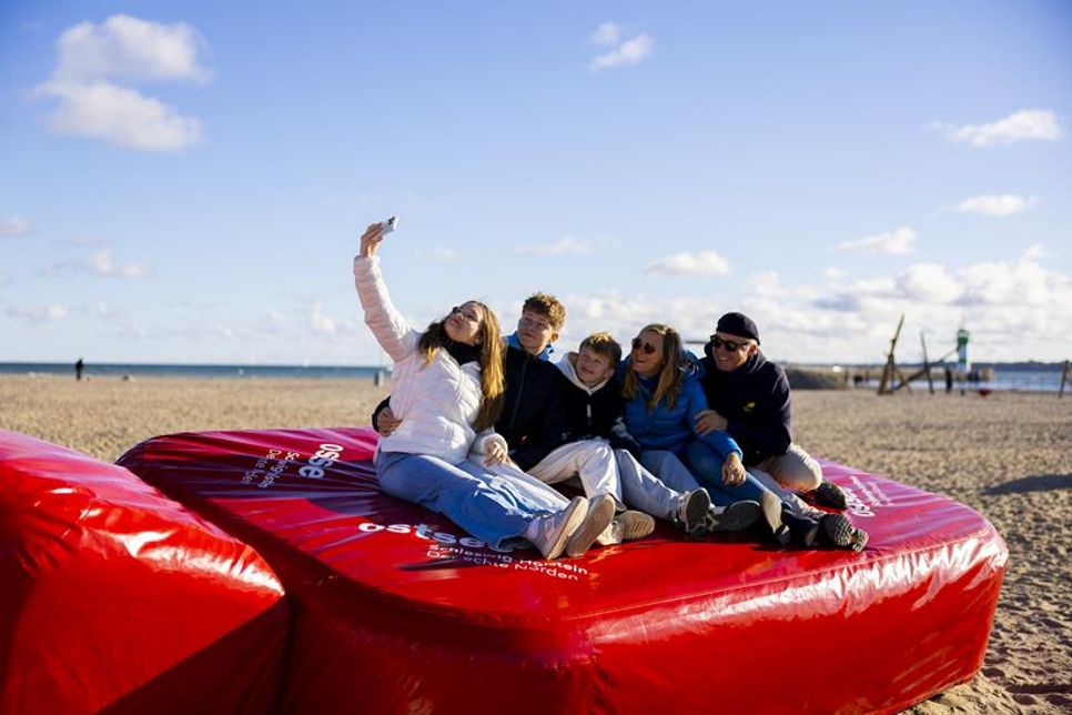 Eine Familie erkundet die Riesenwärmflasche am Ostseestrand. (Foto: www.ostsee-schleswig-holstein.de)
