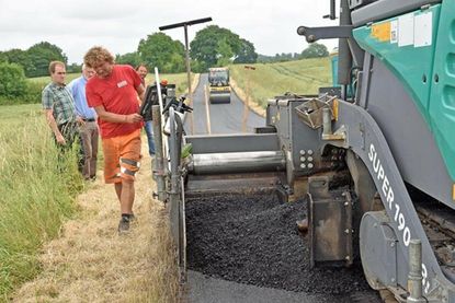Fließende Übergänge: gut isolierte Lkw liefern im Wechsel heißen Teer für die Straße Darland in der Gemeinde Mucheln an, auf der eine neue Decke aufgetragen wird.