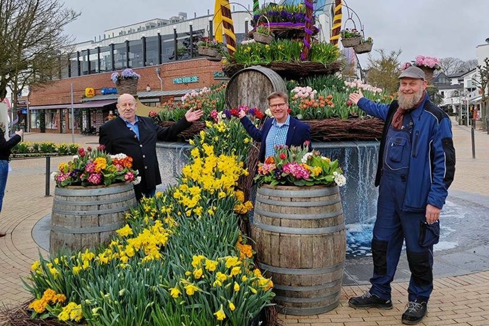 Der bunte Osterbrunnen auf dem Timmendorfer Platz mit Wolfgang Rahlf (links), Tourismuschef Joachim Nitz (Mitte) und Sven Petersen vom Bauhof der Gemeinde.
