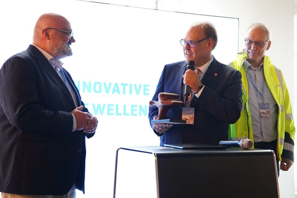 Mirko Spieckermann übergab eine symbolische Welle aus Holz an Akteure anderer Meerwasser-Wärmepumpen-Projekte: Kiels Stadtrat Sascha Thümmler (lks.) und Geschäftsbereichsleiter der Stadtwerke Flensburg Andreas Weckesser (2. v. re.).