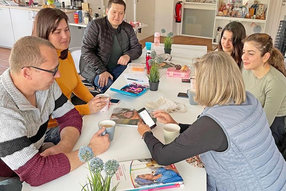 Männer und Frauen aus verschiedenen Nationen unterhalten sich bei einer Tasse Kaffee. Wenn Wörter fehlen, hilft das Smartphone beim Übersetzen.