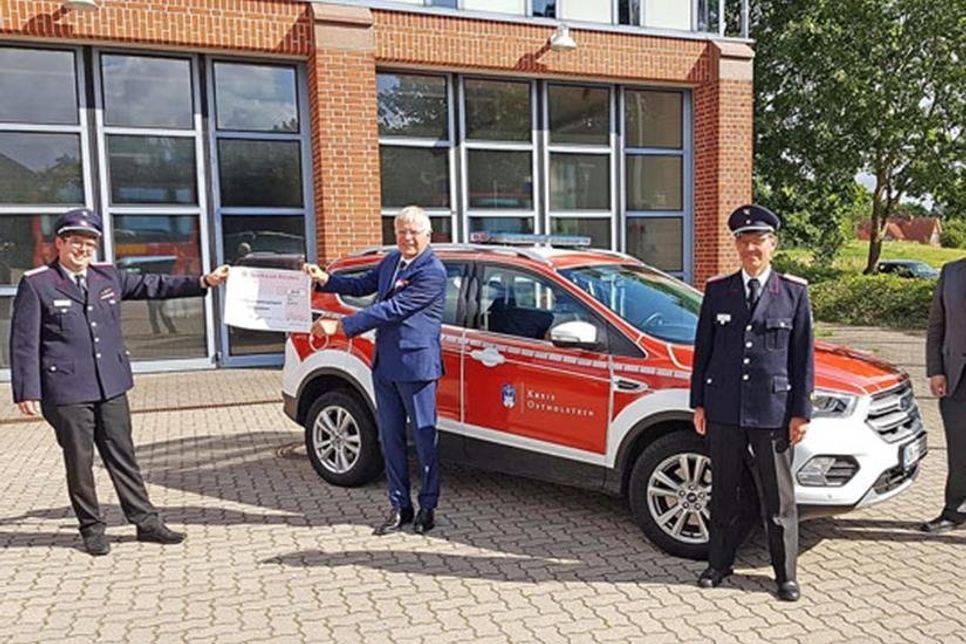 Kreisjugendfeuerwehrwart Jan Klein, Landrat Reinhard Sager, Michael Hasselmann vom Kreisfeuerwehrverband Ostholstein und Jens Meyer von der EGOH bei der symbolischen Scheckübergabe vor der Feuerwehrtechnischen Zentrale des Kreises Ostholstein in Lensahn.