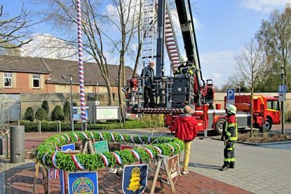 Noch liegt der Maikranz noch auf vier Böcken. Feuerwehrmann Till Arens und Bürgervorsteher Ernst-Peter Schütt (im Korb) sowie Löschmeister Michael Knickrehm und HGV-Vorstandsmitglied Josef Pollmann kümmern sich um die Aufhängung.