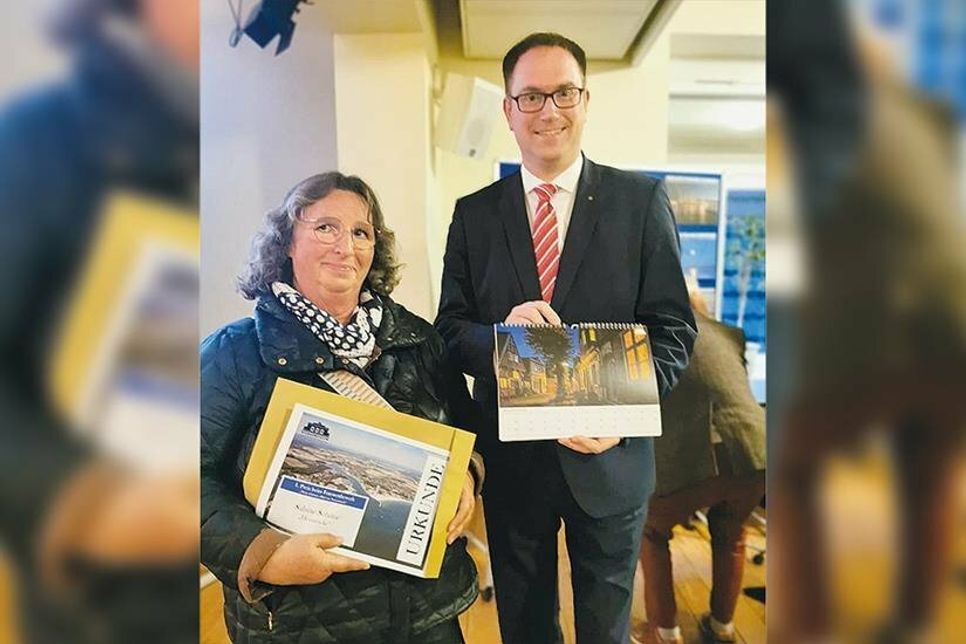 Sabine Schöne, Gewinnerin des Fotowettbewerbes, mit Lübecks Bürgermeister Jan Lindenau, der den Kalender des Wettbewerbs in der Hand hält.