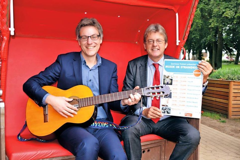 André Rosinski (links mit Gitarre) und Hans-Ingo Gerwanski von der Sparkasse Holstein haben schon einmal im Strandkorb Platz genommen und freuen sich auf die Veranstaltungsreihe „Musik im Strandkorb“. (Foto: René Kleinschmidt)