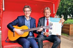 André Rosinski (links mit Gitarre) und Hans-Ingo Gerwanski von der Sparkasse Holstein haben schon einmal im Strandkorb Platz genommen und freuen sich auf die Veranstaltungsreihe „Musik im Strandkorb“. (Foto: René Kleinschmidt)