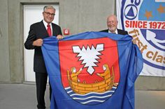 „Eine wundervolle Geste“, nannte Oliver Seiter (lks.) das Geschenk der Stadt Neustadt. Bürgervorsteher Sönke Sela übergab eine Neustadt-Flagge.