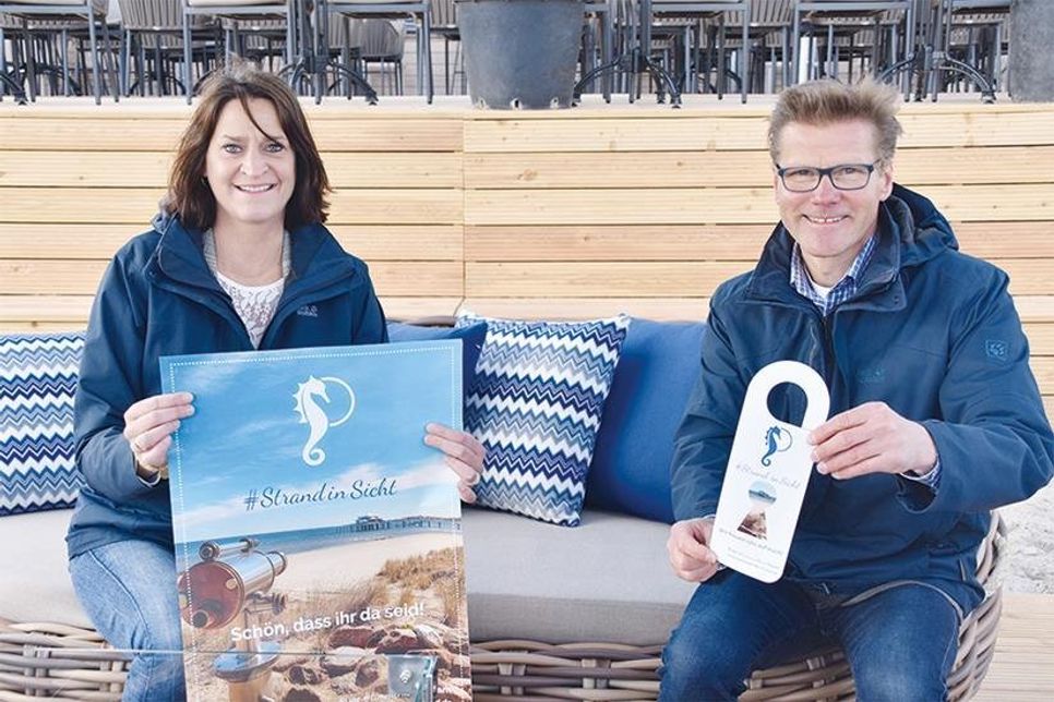 Timmendorfer Strands Marketingleiterin Silke Szymoniak und Tourismuschef Joachim Nitz präsentieren die Plakate und Türhänger mit der Aufschrift „Strand in Sicht – Schön, dass ihr da seid“, die zur Gäste-Begrüßung hergestellt wurden und von der TSNT GmbH kostenlos an die Betriebe gegeben werden.
