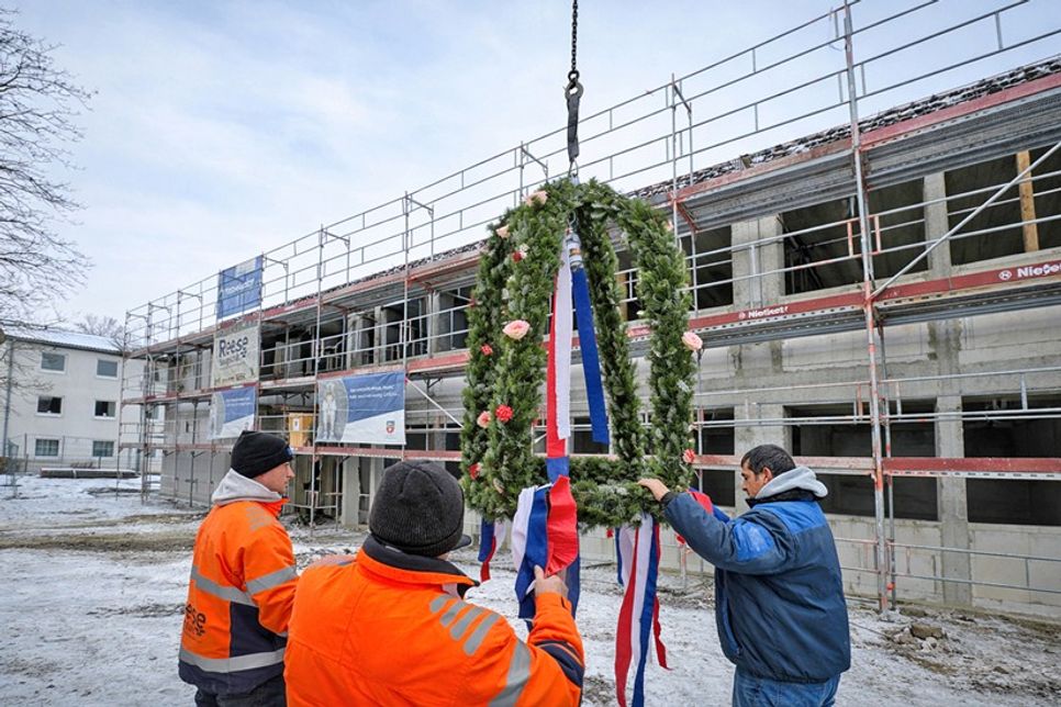 Kein Richtfest ohne Krone: Der Kranz, den die Mitarbeiter der Baufirma Reese hier am Kran befestigen, wurde von der Gärtnerei Möller gebunden.