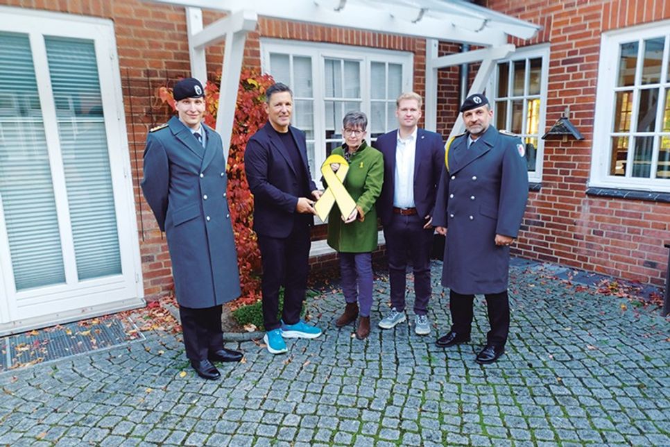 Die Eutinerin Christine Dunker-Kobza übergibt im Beisein von Kompaniechef Hauptmann Max Adrian (li.) und „Spieß“ Oberstabsfeldwebel Dirk Reichenbach (re.) die gelbe Schleife an Bürgermeister Thomas Keller (2.v.li.) und Bürgervorsteher Daniel Thomaschewski.