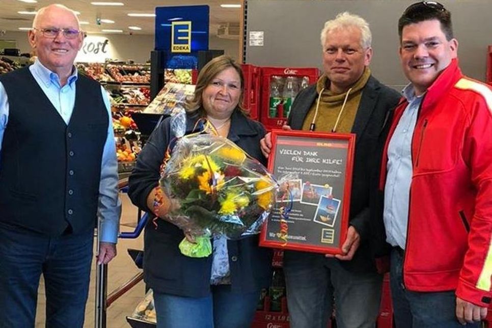 Jürgen Schlünder (DLRG Dahme e.V.) mit Betreiber-Ehepaar Weinberg und Thies O. Wolfhagen (DLRG LV SH): Blumen als Dank für die Unterstützung und ein neues Plakat für den Spender/innen: 5.555 Euro