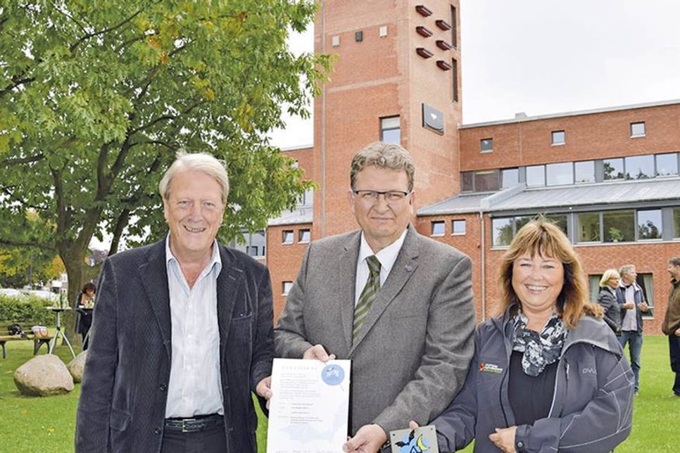 Christian Dwars (Mitte), stellvertretender Bürgermeister der Gemeinde Scharbeutz, erhält von Sandra Redmann und Hermann Schultz Plakette und Urkunde, im Hintergrund der Turm mit den Installationen für die Fledermäuse. (Foto: Eknad)