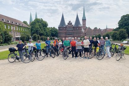 Die Teilnehmenden der Radtour des Gemeinnützigen Bürgervereins Bad Schwartau überreichen vor dem Holstentor in Lübeck den Staffelstab an Sophia Cornelißen, Klimaschutzmanagerin der Gemeinde Stockelsdorf.
