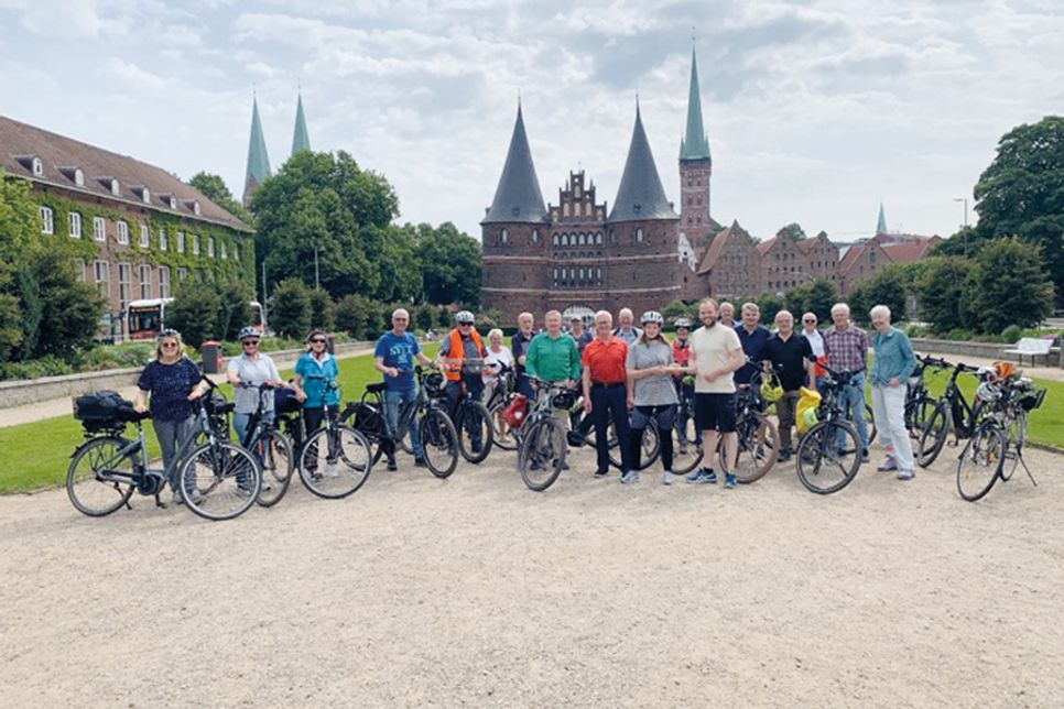 Die Teilnehmenden der Radtour des Gemeinnützigen Bürgervereins Bad Schwartau überreichen vor dem Holstentor in Lübeck den Staffelstab an Sophia Cornelißen, Klimaschutzmanagerin der Gemeinde Stockelsdorf.
