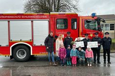 Mike und Swantje Wulf mit Volker Langbehn, stellvertretender Kindergartenleitung Sylke Vogt, weiteren Feuerwehrmännern (v. lks.) und Kindergartenkindern bei der Spendenübergabe in Grube.