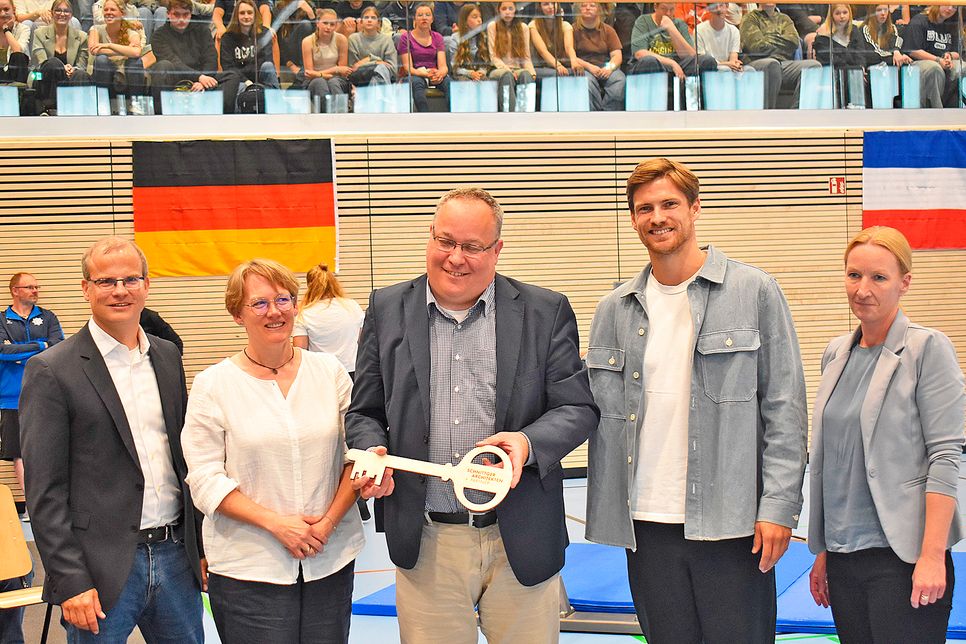 Schulverbandsvorsteher Lutz Schlünsen (m.) hält voller Stolz den Schlüssel für die neue Sporthalle in seinen Händen. Eingerahmt wird er von Markus Oddey (GSP, l.), Liv Tümmler (Grundschule an den Salzwiesen, 2.v.l), Rune Dahmke (2.v.r.) und Bente Vierck (Architektin, r.)