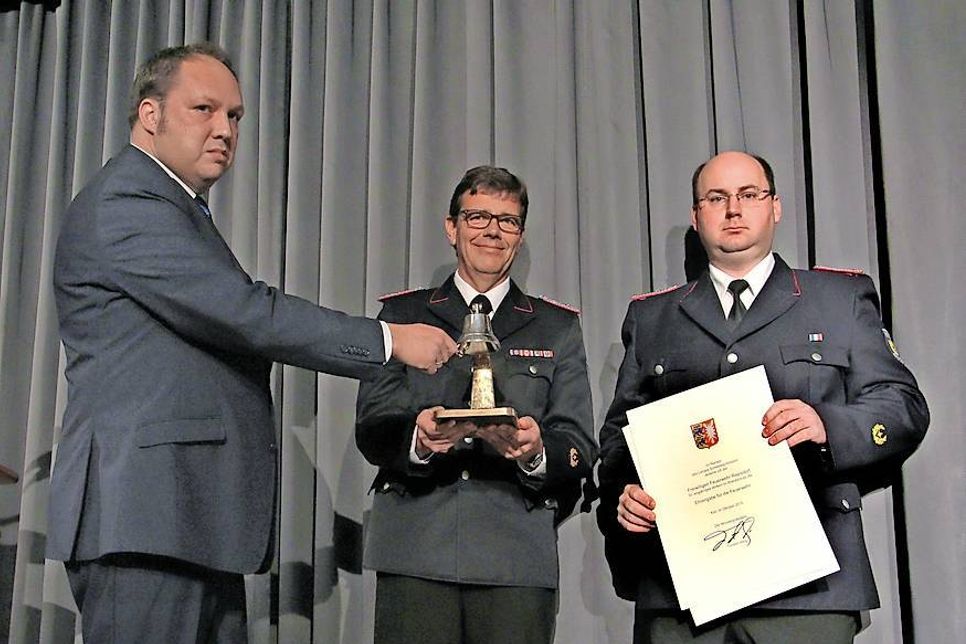 Überreichte die Silberne Glocke als Ehrengabe des Landes Schleswig-Holstein und läutete damit die nächsten 125 Jahre ein: der stellvertretende Landrat Timo Gaarz mit Michael Hasselmann vom Kreisfeuerwehrverband und Ortswehrführer Bastian Bendfeldt (v. lks.).