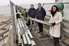 Thomas Albertin (Bauamt der Gemeinde Scharbeutz, links), TALB-Vorstand André Rosinski und Bürgermeisterin Bettina Schäfer mit einer bereits abmontierten Holzplanke, die man mit Glück als Erinnerungsstück erhalten kann.