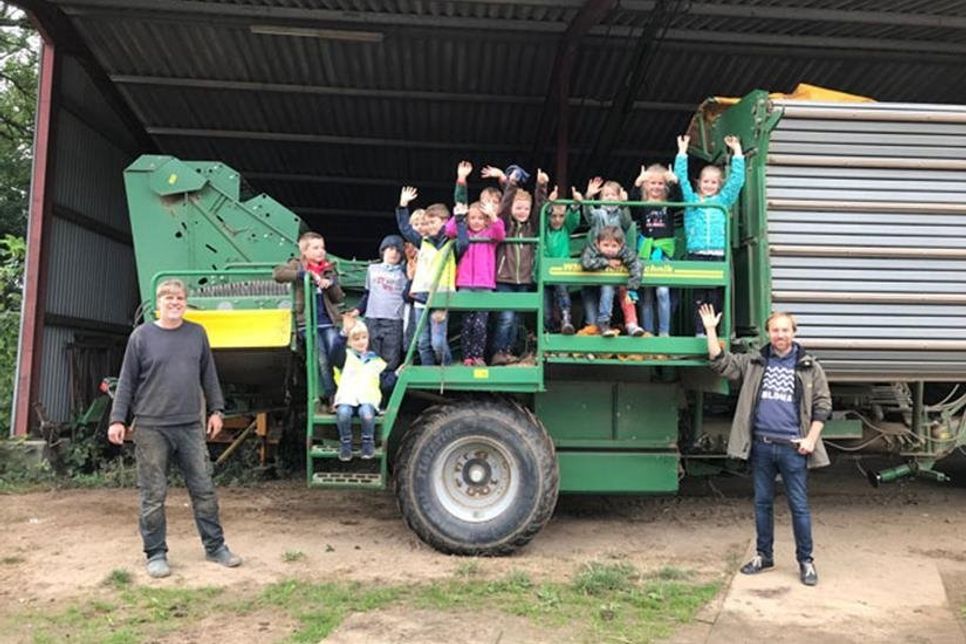 Ein Teil der Klasse winkt begeistert vom Kartoffelroder. Links steht Hofbesitzer Wolf-Heinrich Schumacher und rechts Referendar Christian Frahm.