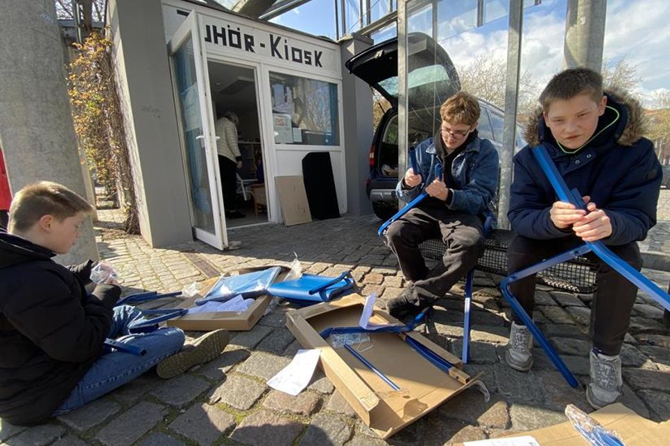 Hand in Hand für die Zukunft: Drei am Projekt beteiligte Jugendliche bauen vor dem Zuhörkiosk Mobiliar für die Ideenwerkstatt zusammen, die künftig hier ihre Tür öffnet.