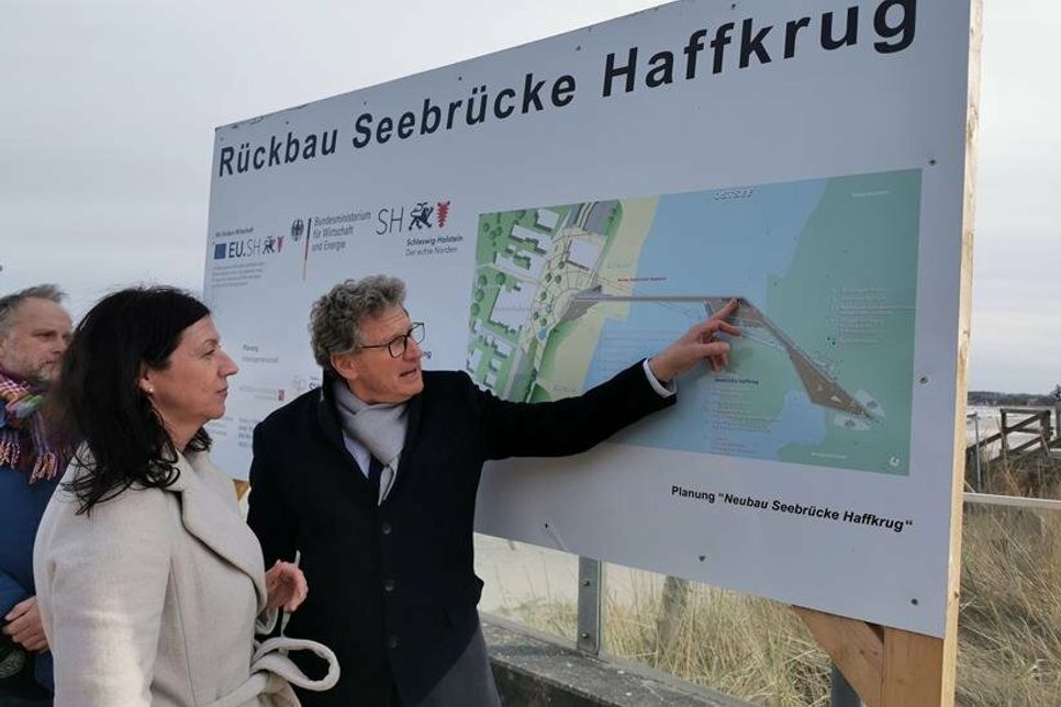Bettina Schäfer, Bürgermeisterin der Gemeinde Scharbeutz, schaut sich mit Minister Dr. Bernd Buchholz die Bau-Tafel der neuen Seebrücke an. (Foto: René Kleinschmidt)