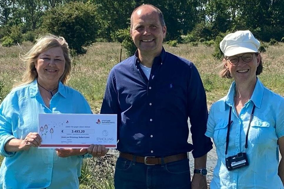 Sandra Redmann Vorstandsvorsitzende der Stiftung Naturschutz Schleswig-Holstein nimmt die großzügige Spende von knapp 3.500 Euro aus den Händen des Hoteliers Markus Schnoor entgegen. Flächenmanagerin Heike Henning führte die Beiden über die bunte Vielfalts-WG, einen Steinwurf vom Hotel „Erholung“ entfernt.