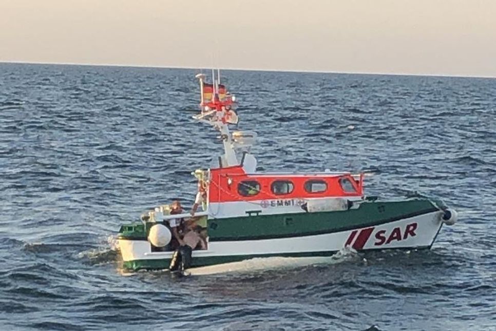 Nur mit einer Badehose bekleidet wird einer der beiden Schiffbrüchigen von Seenotrettern auf dem Tochterboot „Emmi“ des Seenotrettungskreuzers „Hans Hackmack“ aus dem Wasser gezogen. Der andere Mann wurde bereits gerettet. Vor dem Tochterboot ist die gekenterte Jolle zu erkennen. (Copyright DGzRS - Die Seenotretter)