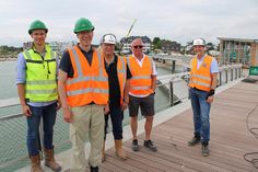 Sebastian Beckmannshagen (von links) und Karl Hellmigk (beide Otto Wulff), Jörg Ferwerda (Heuvelmann-Ibis GmbH), Frank Helmke (C+P Brückenbau GmbH) und Bauherrenvertreter Dirk Dibbern auf der Seebrücke in Haffkrug, im Hintergrund der fertiggestellte Sportbootsanleger.