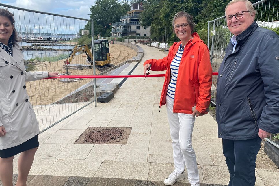 Band durchtrennt, doch die Promenade bleibt vorerst geschlossen: Hilla Mersmann nimmt’s mit Humor und eröffnet symbolisch, flankiert von Juliane Bohrer und Werner Kalinka.