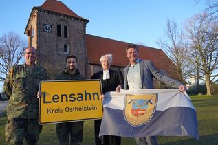 Das Ortsschild der Gemeinde Lensahn geht mit in den Kosovo, während die Kompaniefahne in der Zeit des Einsatzes vor dem Lensahner Rathaus weht. Den Tausch vollzogen stellvertretender Kompaniechef Ulf Hadeler, Kompaniechef David Cacic, Vertretungspastor im Kirchspiel Bungsberg Jens Motschmann sowie Bürgermeister Michael Robien (v. lks.).