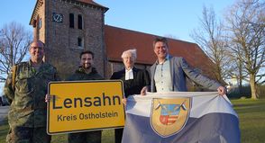 Das Ortsschild der Gemeinde Lensahn geht mit in den Kosovo, während die Kompaniefahne in der Zeit des Einsatzes vor dem Lensahner Rathaus weht. Den Tausch vollzogen stellvertretender Kompaniechef Ulf Hadeler, Kompaniechef David Cacic, Vertretungspastor im Kirchspiel Bungsberg Jens Motschmann sowie Bürgermeister Michael Robien (v. lks.).