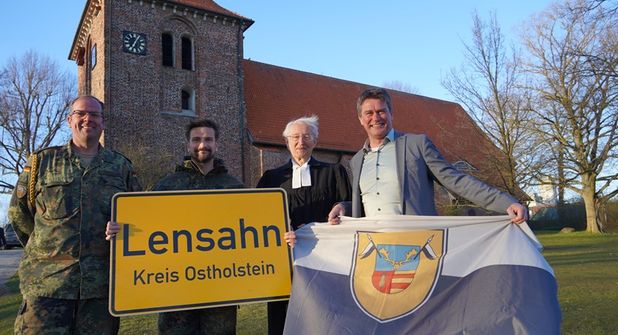 Das Ortsschild der Gemeinde Lensahn geht mit in den Kosovo, während die Kompaniefahne in der Zeit des Einsatzes vor dem Lensahner Rathaus weht. Den Tausch vollzogen stellvertretender Kompaniechef Ulf Hadeler, Kompaniechef David Cacic, Vertretungspastor im Kirchspiel Bungsberg Jens Motschmann sowie Bürgermeister Michael Robien (v. lks.).