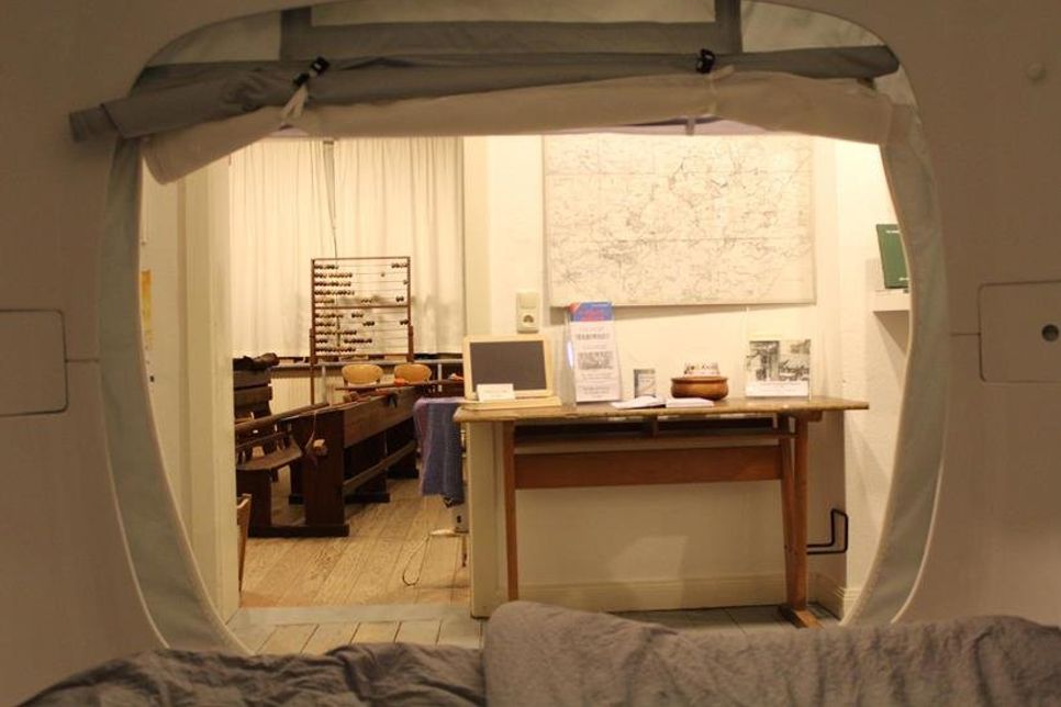 Aus dem gemütlichen „sleep Cube“ schauen die Gäste direkt in das historische Klassenzimmer mit seinen hölzernen Schulbänken, Schiefertafeln und Lehrerpult.