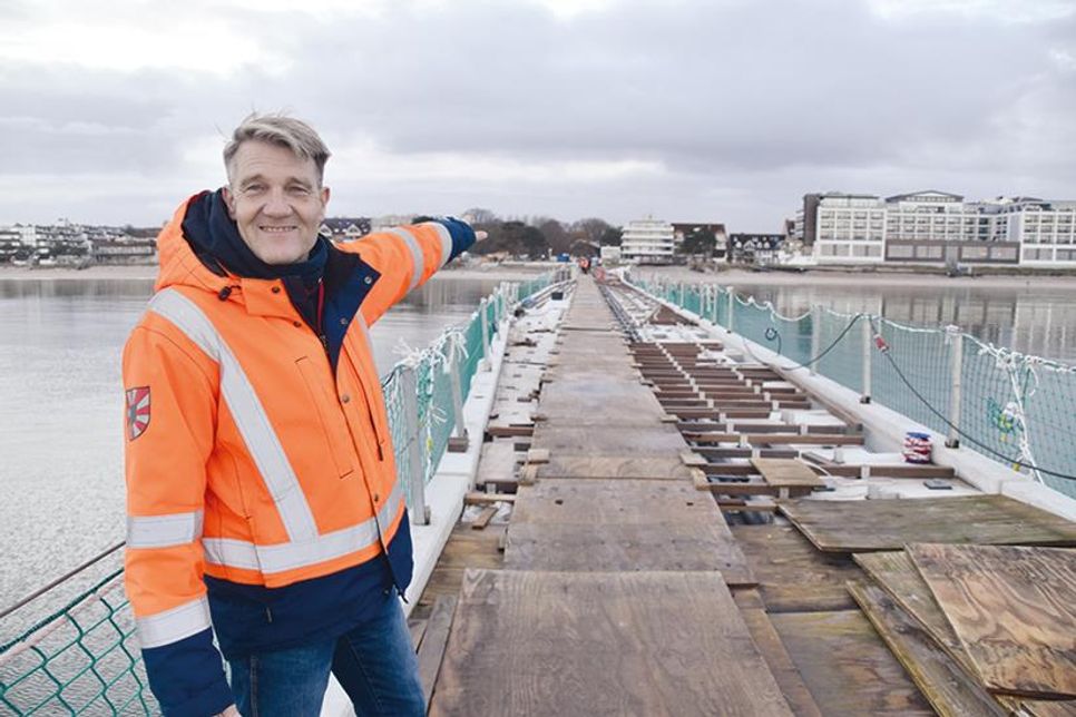 Techniker Dirk Dibbern vom Bauamt der Gemeinde Scharbeutz zeigt auf die im Bau befindliche Seebrücke, auf der jetzt das Belagsholz verlegt und montiert wird.
