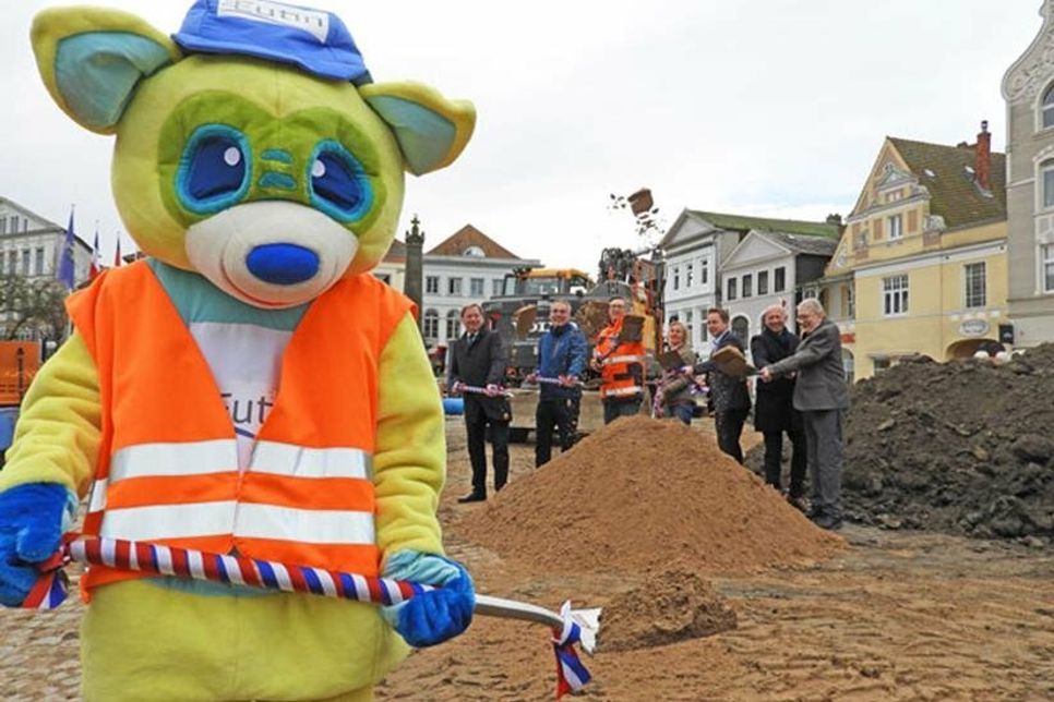 Der Beginn der Bauarbeiten auf dem Eutiner Marktplatz ist seit Mitte Oktober unübersehbar. Jetzt wurde er auch symbolisch begangen – mit einem gemeinsamen Spatenstich von Stadtverwaltung, Politik und der Hauptpersonen, die mit Bagger und Knowhow die Arbeit erledigen. Natürlich war auch Baubär Eu dabei.