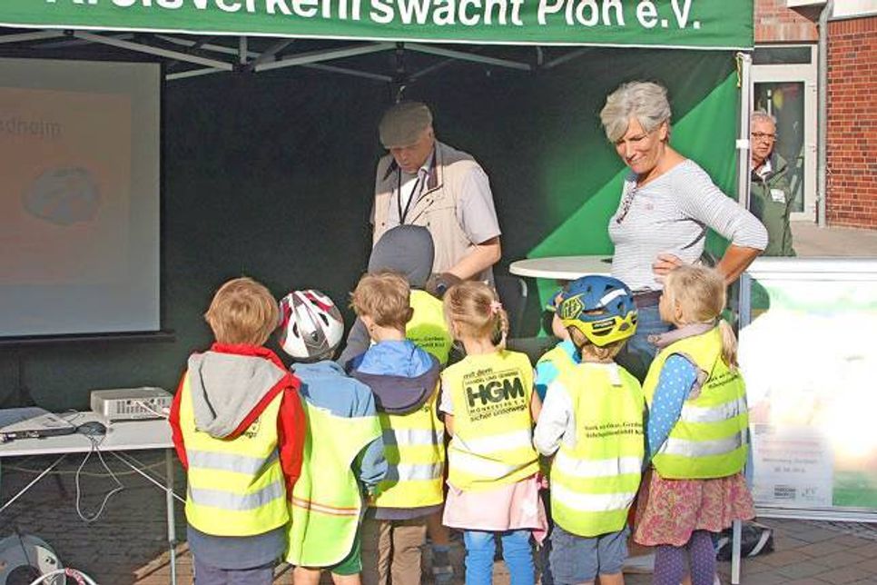 Lachend sitzt die Puppe auf ihrem Sitz. Gleich wird sie einen Verkehrsunfall erleben, der in der Realität für ein Kind vermutlich mit schwersten Verletzungen oder dem Tod enden würde. Bürgermeisterin Hildegard Mersmann und Hans-Dieter Schwarz eröffneten auf dem Mönkeberger Marktplatz den Verkehrssicherheitstag.
