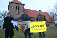 Während das Ortsschild der Gemeinde Lensahn mit in den Kosovo geht, weht die Kompaniefahne während der Zeit des Einsatzes vor dem Lensahner Rathaus. Den Tausch vollzogen Pastor Jörg Reimann, Bürgermeister Michael Robien und Major Jonas Gerwing (v. lks.).