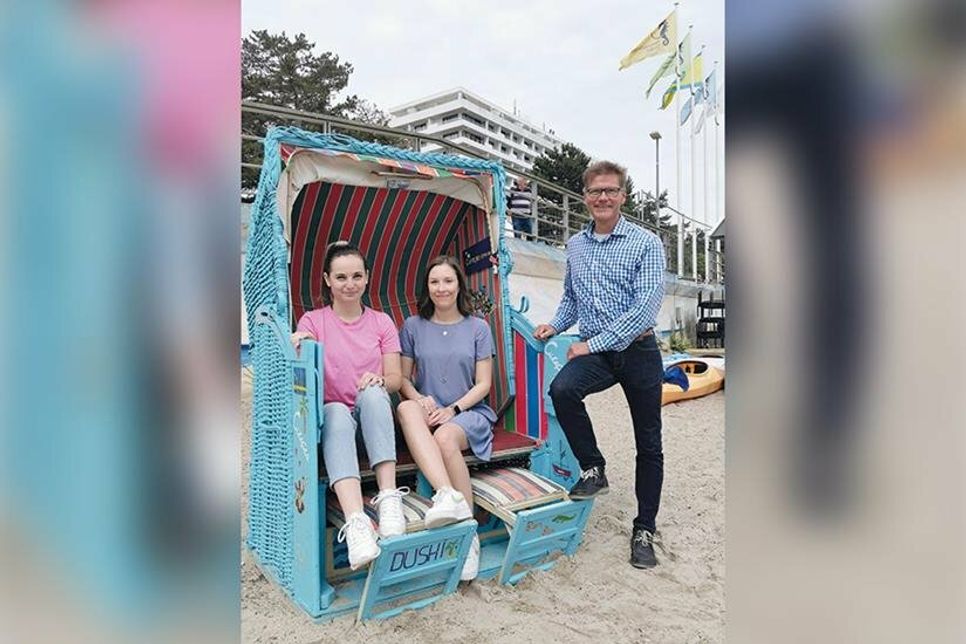 Hannah Block (links) und Lea Muuß aus der Marketingabteilung der TSNT GmbH und Tourismuschef Joachim Nitz mit dem umgestalteten Strandkorb, der jetzt als Fotomotiv für das Gewinnspiel am Timmendorfer Sportstrand platziert wurde.