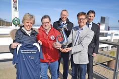 Sabine Bremeyer und Udo Brechtel vom NTSV präsentieren mit Tourismuschef Joachim Nitz das Laufshirt und einen der begehrten Seepferdchen-Pokale, sehr zur Freude von Fred Bobsin (hi.li.) und Volker Schinkewitz von der Sparkasse Holstein. (Foto: René Kleinschmidt)