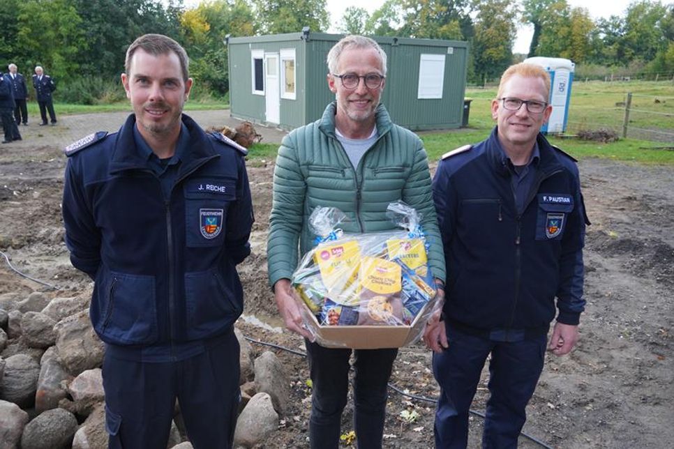 Für seine Spende bedankten sich Frank Paustian (re.) und Jan Reiche (lks.) mit einem Präsentkorb bei Hinrich Behrens. Im Hintergrund die beiden Container.