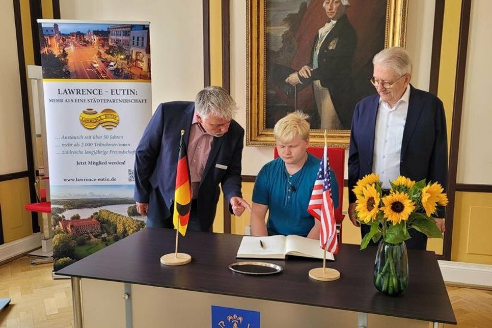 Bürgermeister Sven Radestock (links) und Bürgervorsteher Dieter Holst (rechts) zeigen einem amerikanischen Schüler das Gästebuch der Stadt