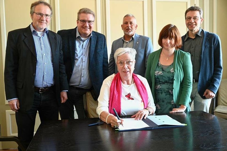 Pastor Ulf Teichmann (in Vertretung für den KGR-Vorsitzenden Jörn Lauenroth), Propst Dirk Süssenbach, Bürgermeister Jörg Saba, Heike Steinbach und Dr. Gerdt Hübner (Stv. Vors. des Fördervereins) (v. lks.). Am Tisch signierend sitzt Beate Rinck, Vorsitzende des Fördervereins. (Foto KKOH/Heinen)
