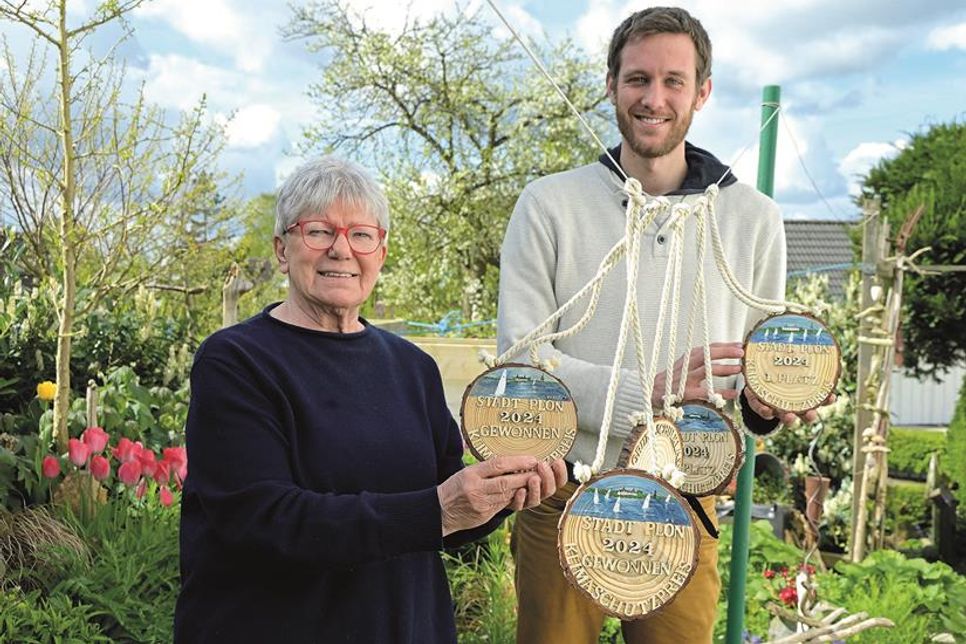 Karin Paprzik, Atelier Grell, und Sebastian Welte, Klimaschutzmanager der Stadt Plön, werben um Einsendungen im Rahmen des Klimaschutzwettbewerbs 2024 – die selbstgebauten und bemalten Medaillen aus Holz aus dem Garten geben ein Beispiel in Sachen Nachhaltigkeit ab