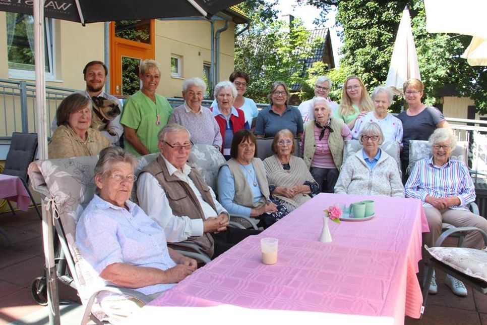 Bewohner und Mitarbeiter der Seniorenpension Erlenkamp genießen gemeinsam die Sonne auf der Terrasse. Im familiären Ambiente fühlen sich alle sichtlich wohl – auch die tierischen Begleiter sind mit dabei.