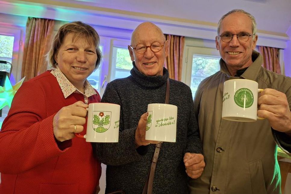 Die stellvertretende Bürgermeisterin Angela Hüttmann sowie Michael Schmidt und Arnd Heling vom Freundeskreis des Pfarrhofs Schönwalde präsentieren die neuen Tassen mit dem Slogan „Gemeinsam leben in Schönwalde“.
