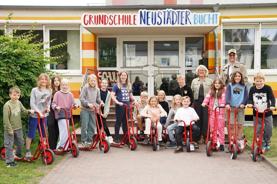 Kevin Neubaumer übergab sieben Roller und zwei Dreiräder an die Grundschule Neustädter Bucht, die die Kinder der Klasse 3e und Schulleiterin Antje Sagawe freudig in Empfang nahmen.