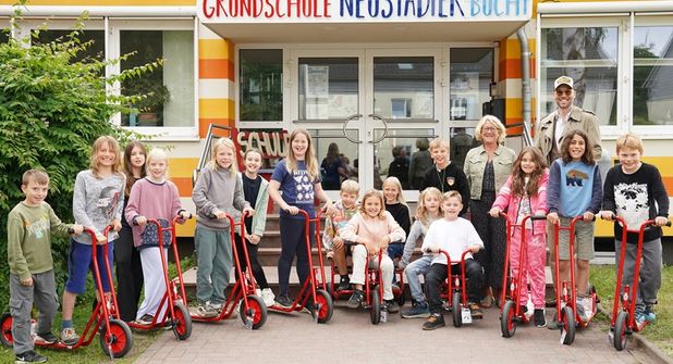 Kevin Neubaumer übergab sieben Roller und zwei Dreiräder an die Grundschule Neustädter Bucht, die die Kinder der Klasse 3e und Schulleiterin Antje Sagawe freudig in Empfang nahmen.