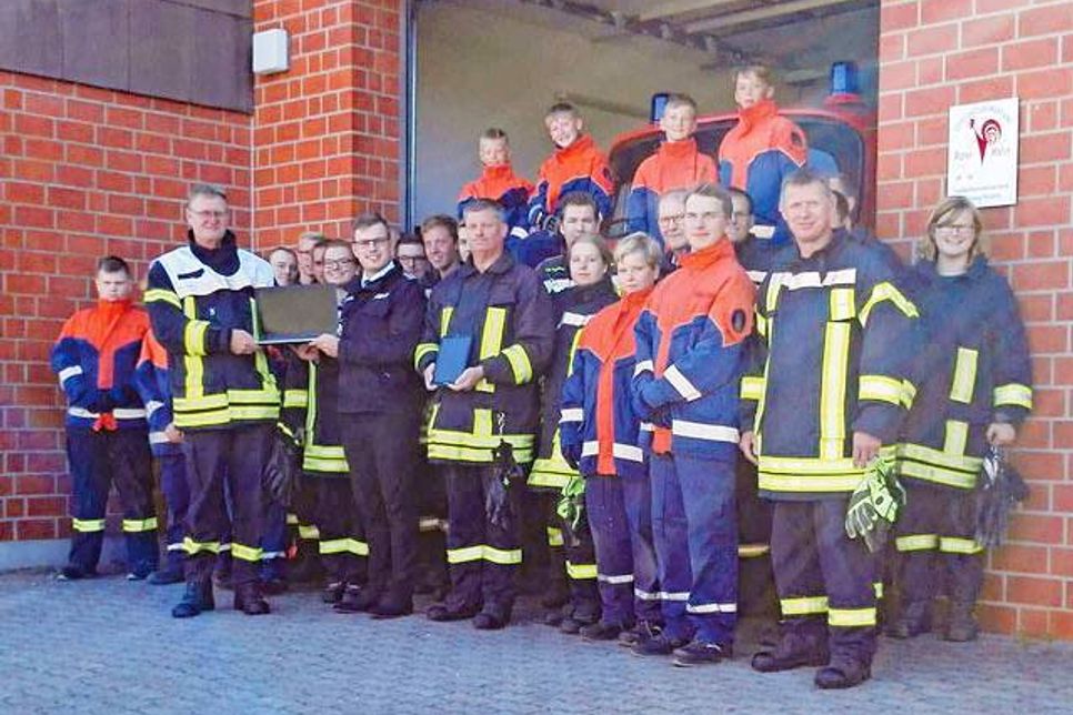Sparkassenmitarbeiter und Feuerwehrmann Daniel Schöning und Gemeindewehrführer Dirk Prüß präsentieren im Beisein der Mitglieder der FFW und der JFW Damlos den neuen Beamer und den neuen Laptop.